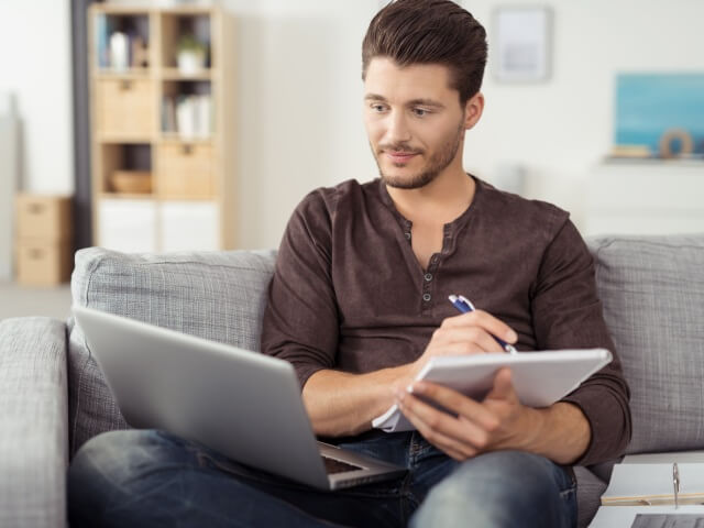 junger Mann macht Notizen auf Sofa