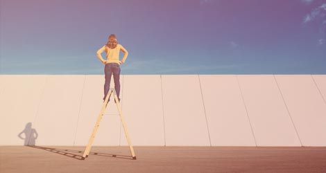 Mensch auf Leiter guckt über Mauer