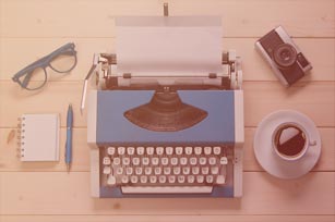 Journalismus Teaser Schreibmaschine auf einem Tisch von oben, darum verteilt eine Tasse Kaffee, ein Notizblock, eine Brille und eine Kamera