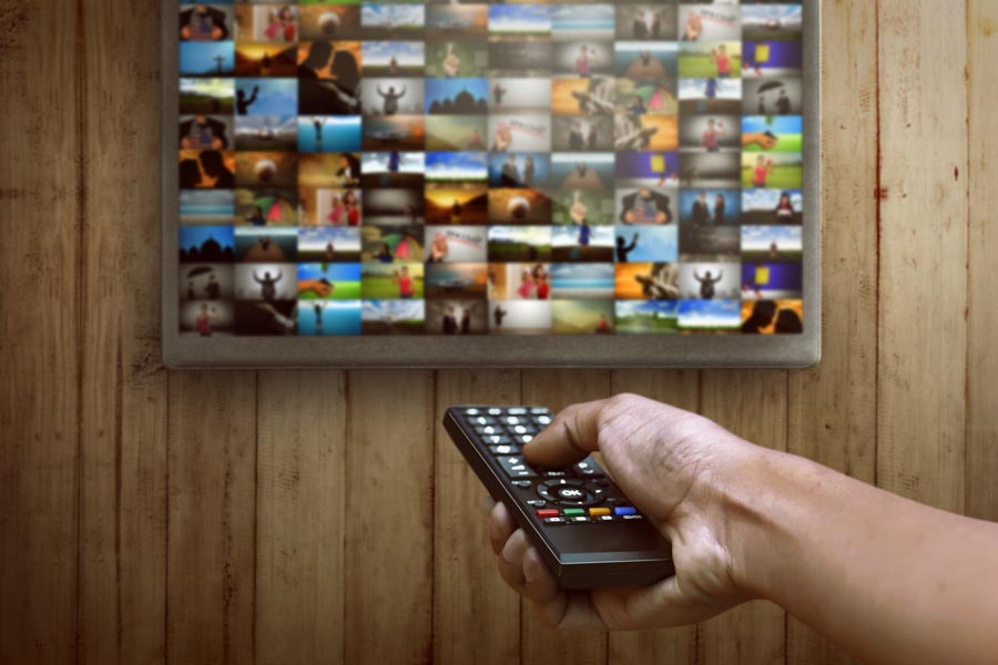 Bildschirm hängt an einer Wand und ein Mann richtet eine Fernbedienung darauf:  ... neuen Formen des Fernsehens, z.B. Smart TVs ...